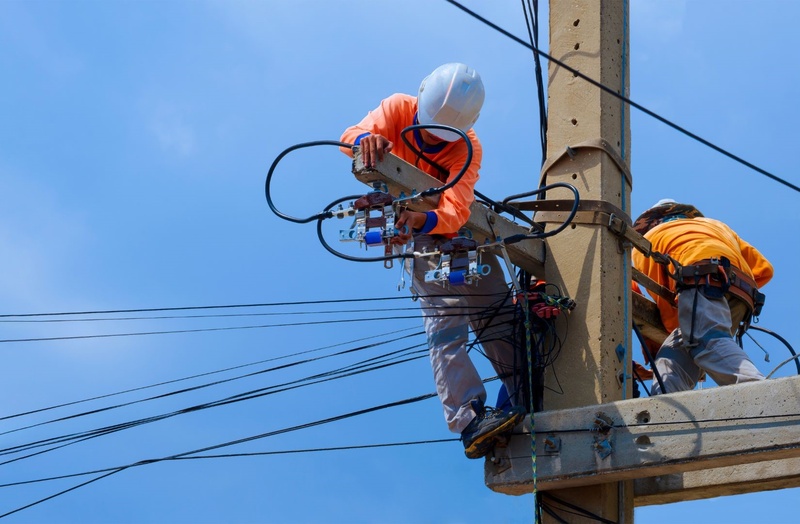 two electricians hanging on an electric pole fixing power lines